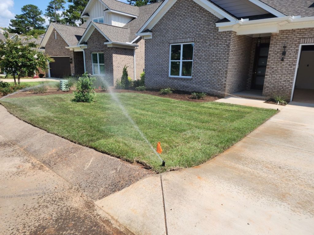 Sprinkler watering a freshly planted front lawn in a residential neighborhood.