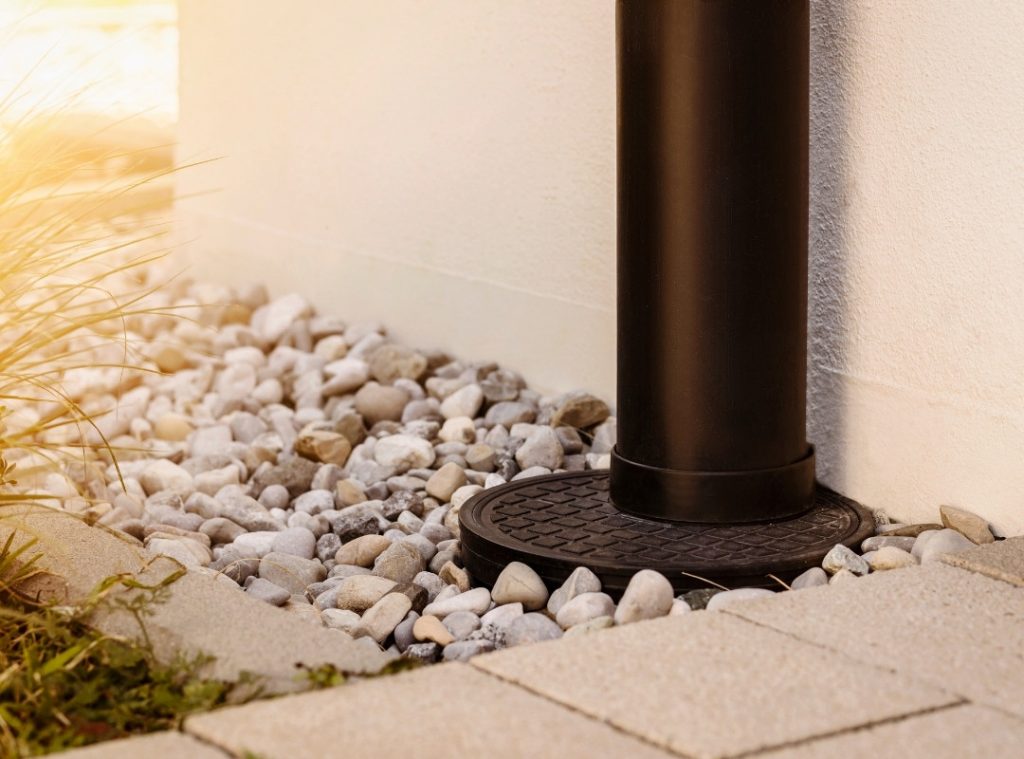 Close-up of a black downspout draining into a gravel bed next to a white building.