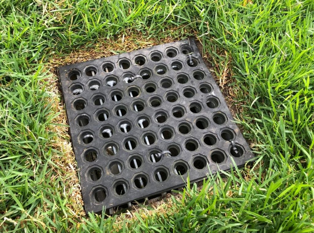 Black plastic drainage grate set into a grassy lawn area.