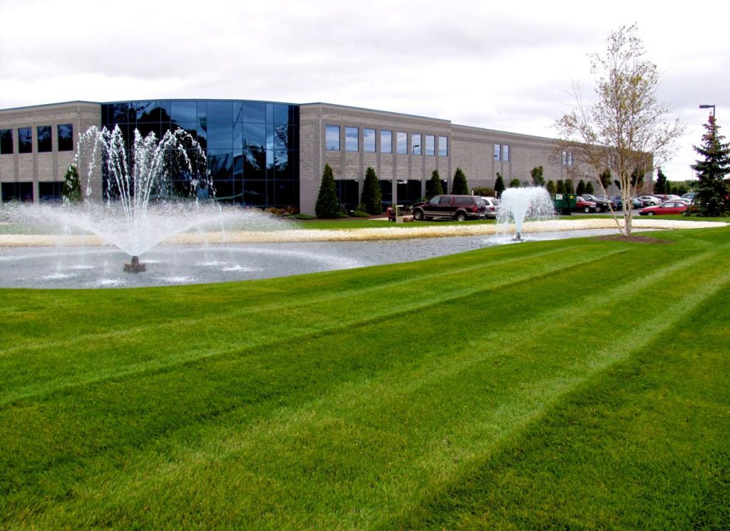 Freshly mowed striped lawn with water fountains in front of a modern commercial building.