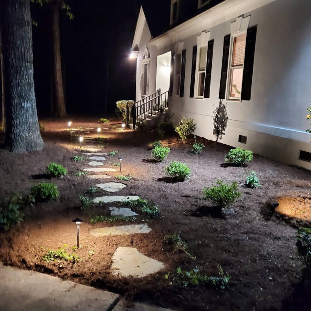 House landscape at night with illuminated stepping stones and garden lighting.
