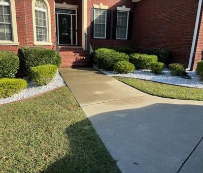 Neatly landscaped front yard with white gravel beds and trimmed bushes. A front yard of a brick house with neatly trimmed bushes and white gravel landscaping beds alongside a curved concrete walkway leading to the entrance.