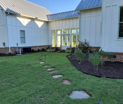Backyard landscaping with stepping stone path and mulched garden beds. A backyard area with a well-manicured lawn, stepping stones forming a path, and a newly mulched flower bed along the house.