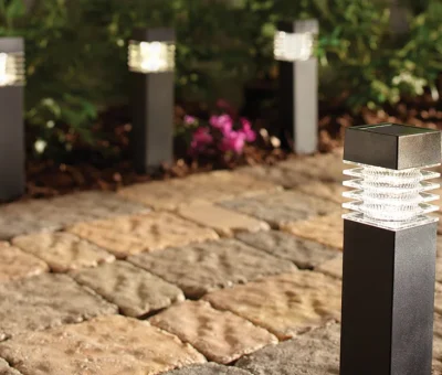 Sleek outdoor lighting along cobblestone garden path. Contemporary garden pathway lights on a cobblestone walkway with greenery and flowers in the background.